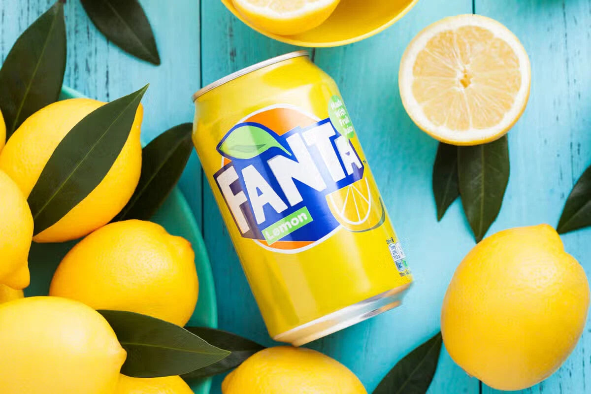 Case of 24 Coca-Cola Fanta Lemon 330ml cans, fizzy soft drinks with bright yellow lemon flavor, stacked in a retail display.